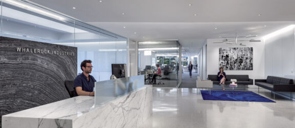 Spacious office lobby with natural light featuring a striking white marble reception desk, minimalist black seating, and modern art. Sleek lines and neutral tones create a welcoming yet professional atmosphere.