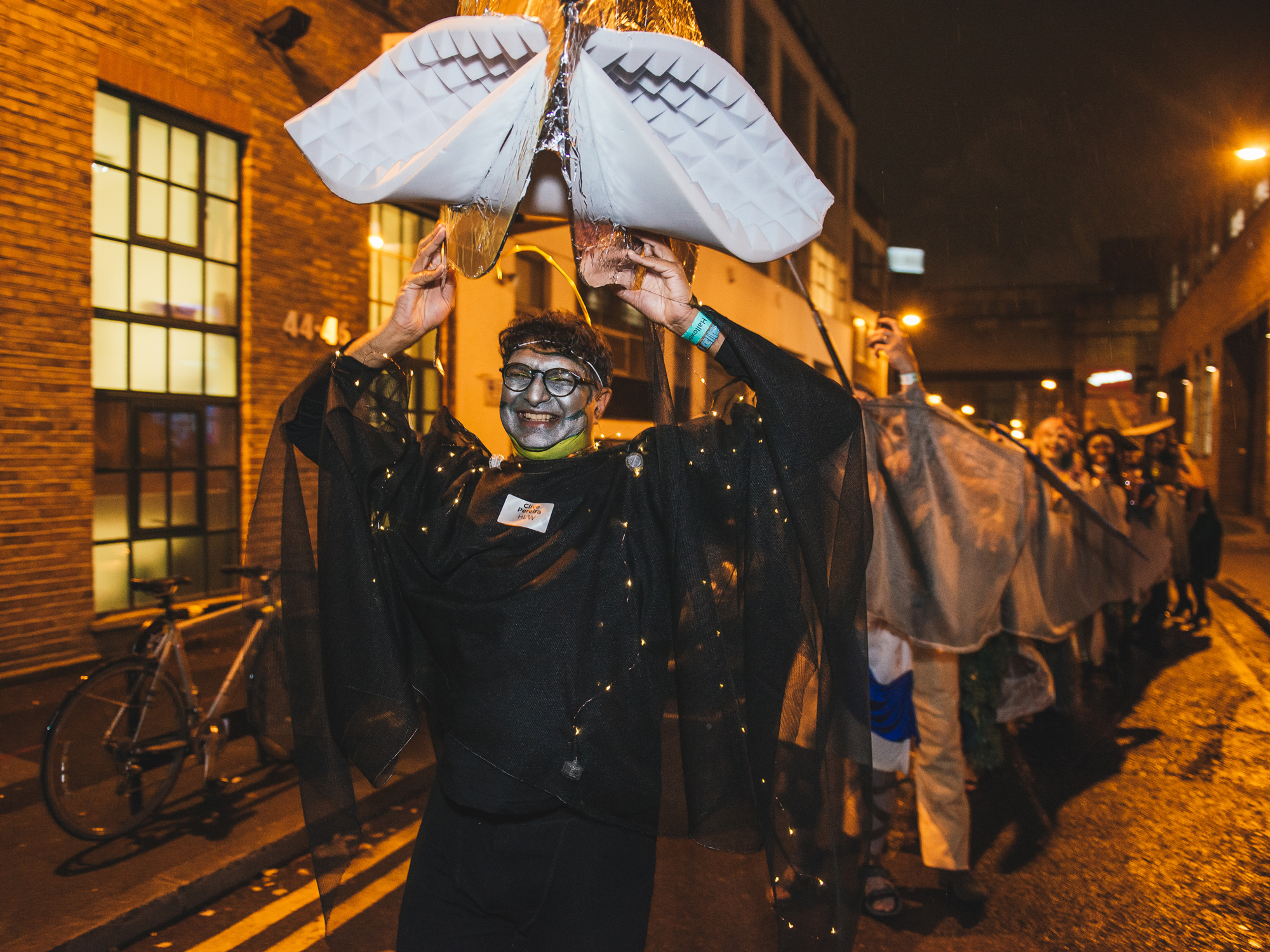 Costumed individual proudly leading a dragon-like ensemble along an urban street.