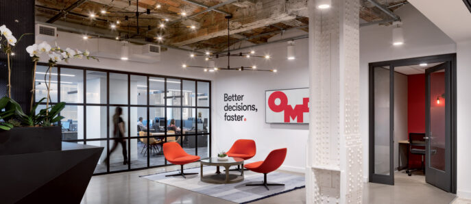 Modern office lounge with eclectic furnishings, featuring an imposing red and white mural, a sculptural white ceiling, and glass pendant lighting. Natural light floods the space, contrasting with the warm wooden floors and creating a dynamic environment for collaboration.