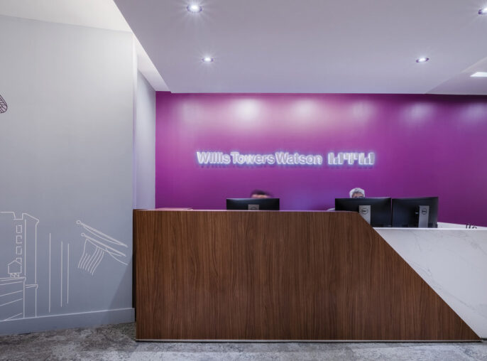 Elegant office lobby featuring a vibrant fuchsia accent wall with Willis Towers Watson branding and a line drawing of a skyscraper, complemented by a sleek, wooden reception desk and modern, recessed ceiling lighting.