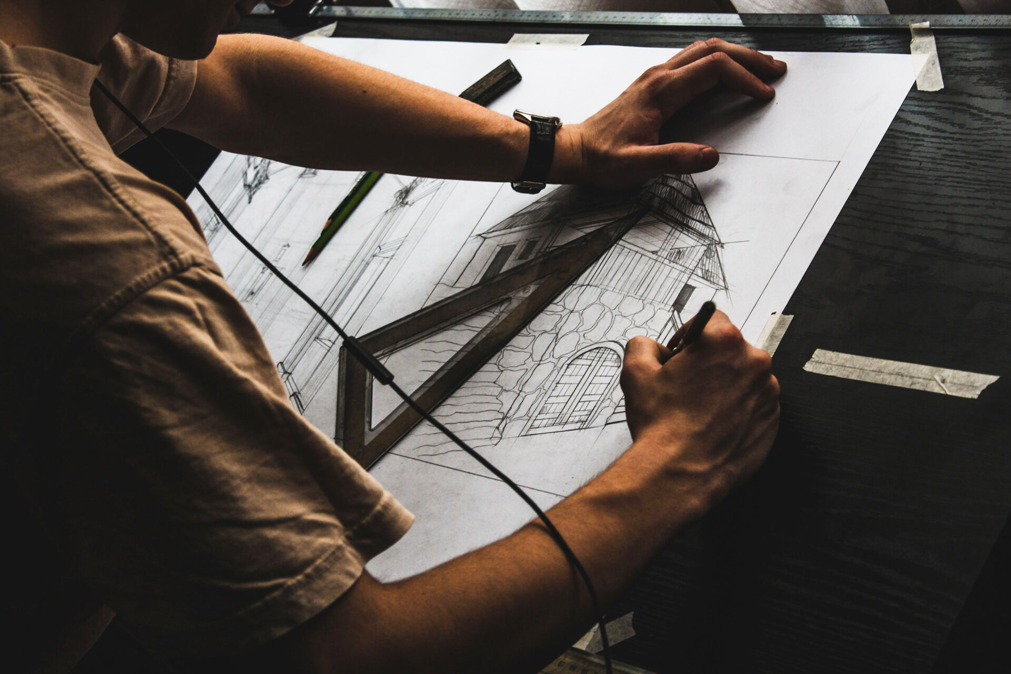 Overhead view of an architect's hands drawing a detailed architectural sketch of a classic house with a gabled roof and arched windows, using a straightedge and pencil on paper, conveying a sense of design precision and creativity.