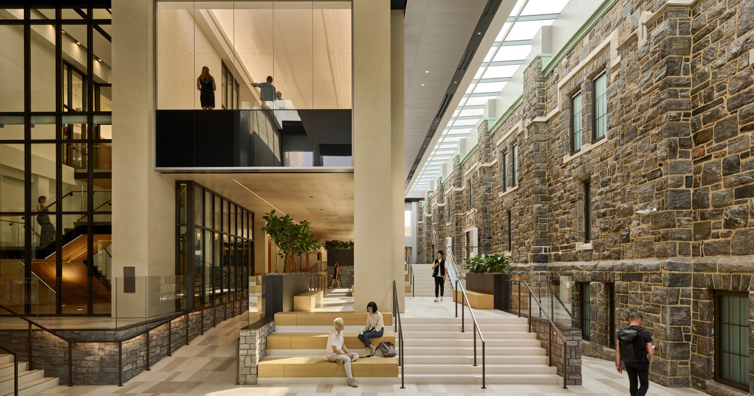 Modern atrium blending contemporary design with classic stone architecture, featuring individuals engaged in various activities throughout the open, sunlit space.