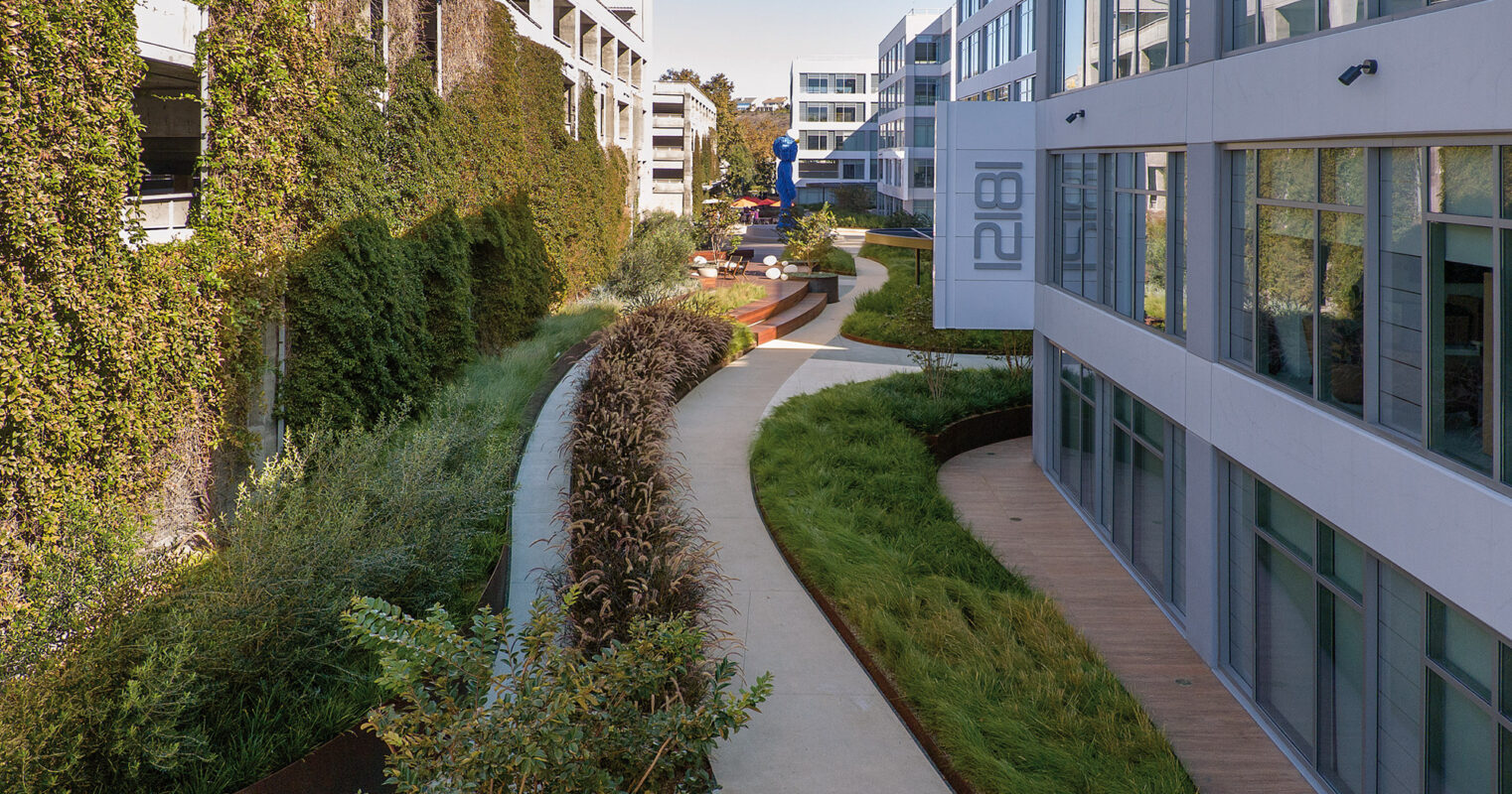 Modern office park with lush green landscaping featuring a winding pathway and contemporary architecture.