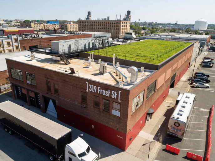 Rooftop urban garden above a brick industrial building, showcasing modern sustainable design with lush greenery against an expansive cityscape background.