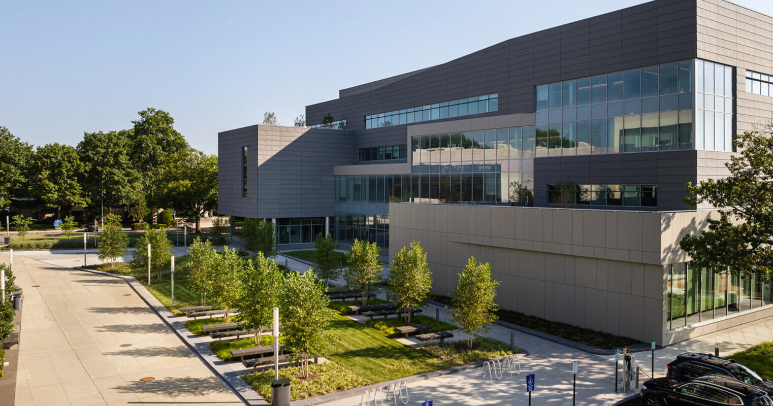 Modern educational building with a sleek design featuring expansive windows and a landscaped approach, with students and visitors making their way along the accessible pathways on a sunny day.