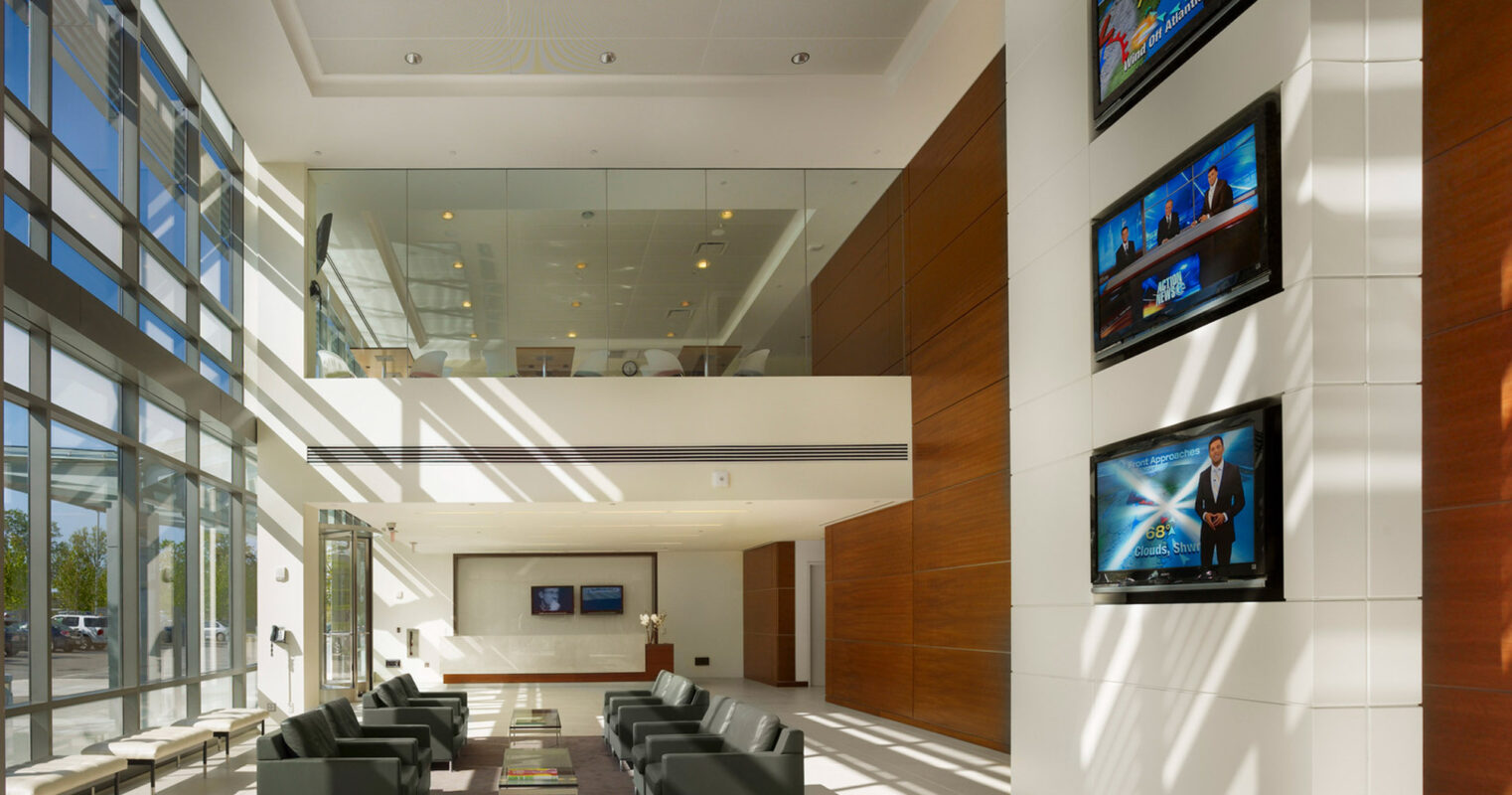 Modern corporate lobby featuring high ceilings with recessed lighting, sleek green armchairs arranged on a marble floor, and wood-paneled walls that complement the neutral color palette, offering a welcoming yet formal ambiance.
