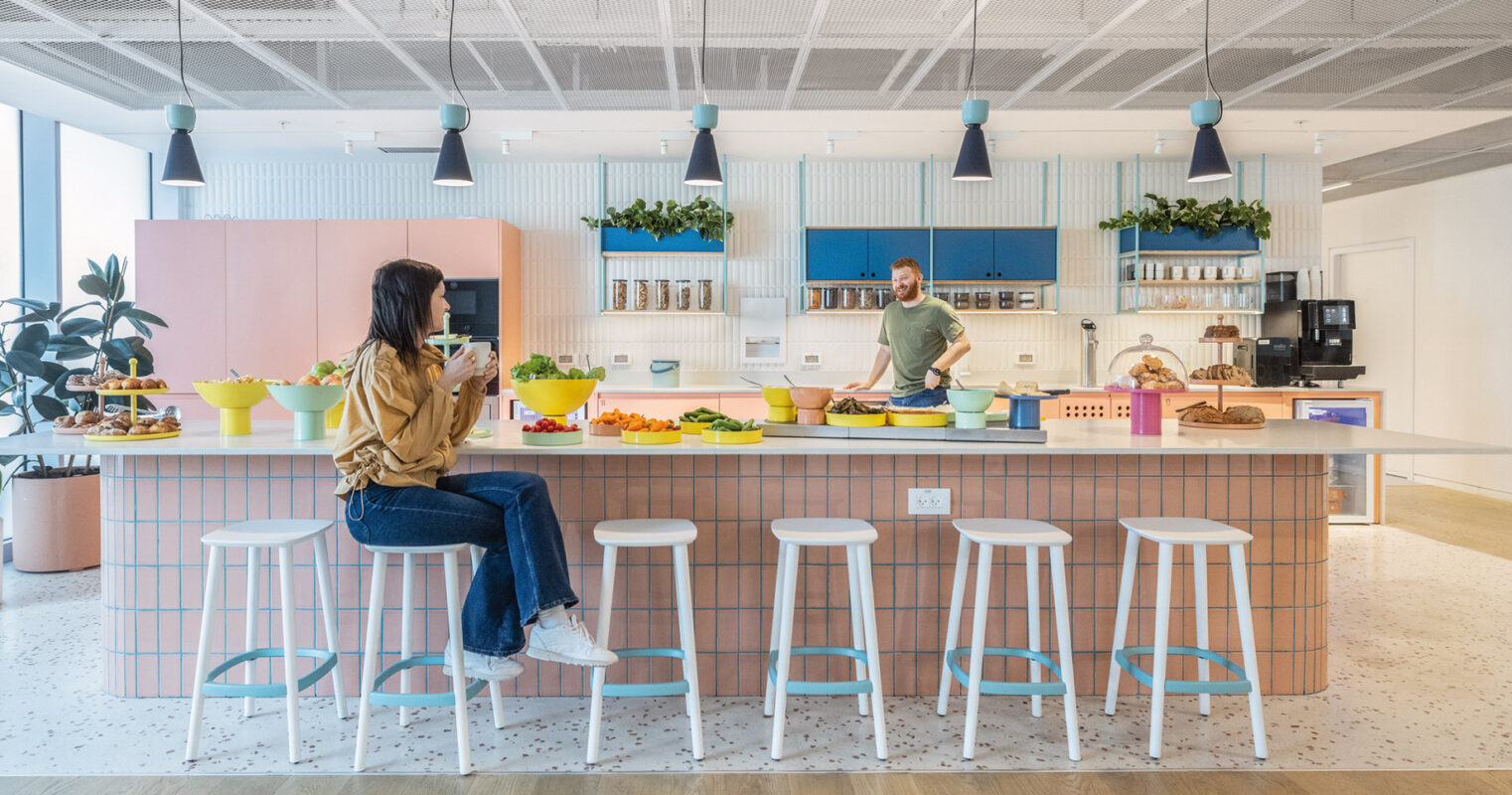 Modern office kitchen area with two people and a variety of salads on the counter.