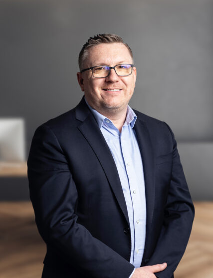 The image portrays a person dressed in business attire, standing against a modern, minimalist background.