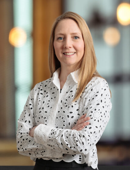 The image features a person wearing a detailed white blouse, standing in a well-lit indoor setting.