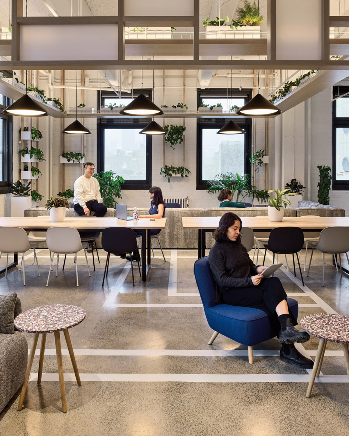 Casual, modern workspace with hanging plants and minial white furniture. People are working on laptops or reading.