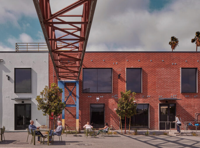 An urban oasis where contemporary architecture meets industrial design, featuring locals enjoying an outdoor seating area under the geometric embrace of an overhead red steel structure, with a serene backdrop of blue skies and palm trees.