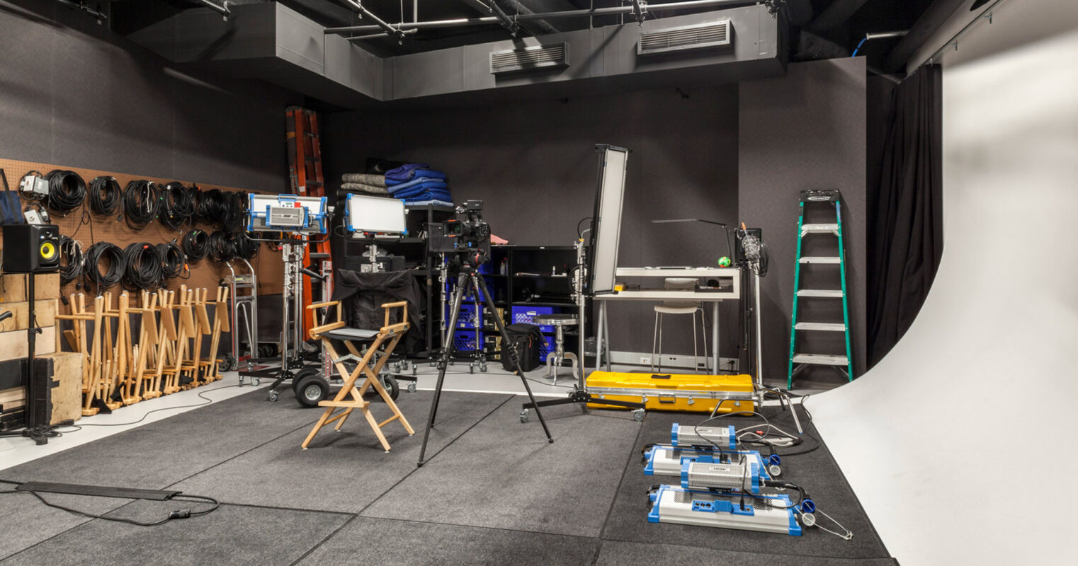 Fully equipped photography studio displaying an organized array of lighting equipment, camera gear, and various props. The space features a seamless white backdrop, a director's chair, and an efficient storage system for equipment, highlighting a functional design that caters to creative workflows.