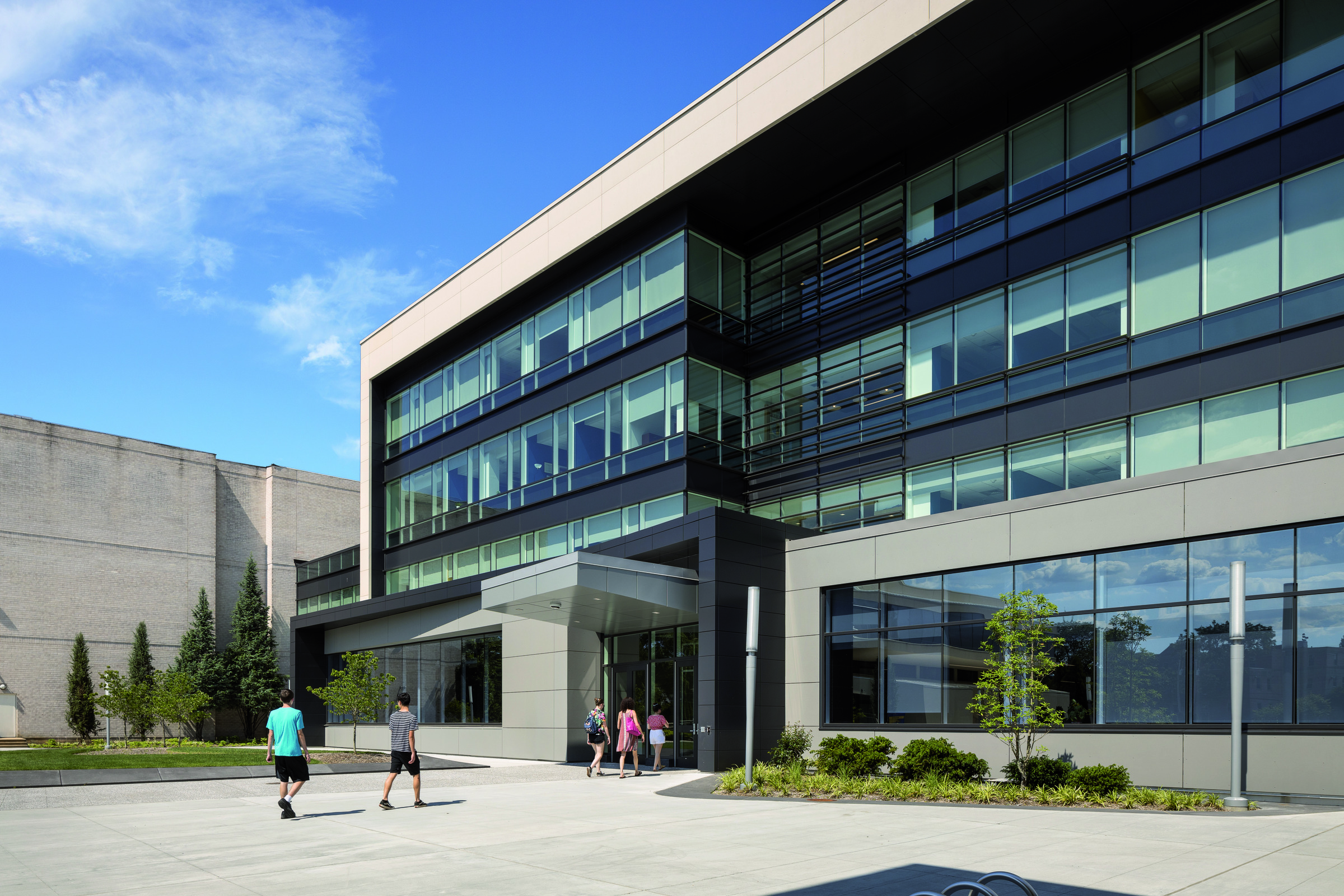 Modern three-story commercial building with an asymmetric facade, featuring a combination of reflective glass windows and pale stone cladding. The ground level’s expansive glazing enhances the indoor-outdoor connection, set against landscaped surroundings.