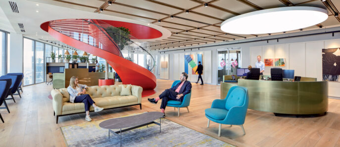 Modern office lobby with natural light, featuring a bold, red spiral staircase as centerpiece. Wood slatted ceiling contrasts with sleek flooring. Curved reception counters and eclectic seating including tufted sofas and vibrant armchairs complete the dynamic space.