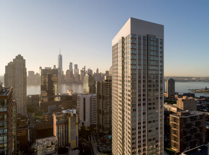 Sunset bathes a modern skyscraper and surrounding cityscape, highlighting the contrast between the glass facade and the urban environment, with a view of a distant iconic tower.