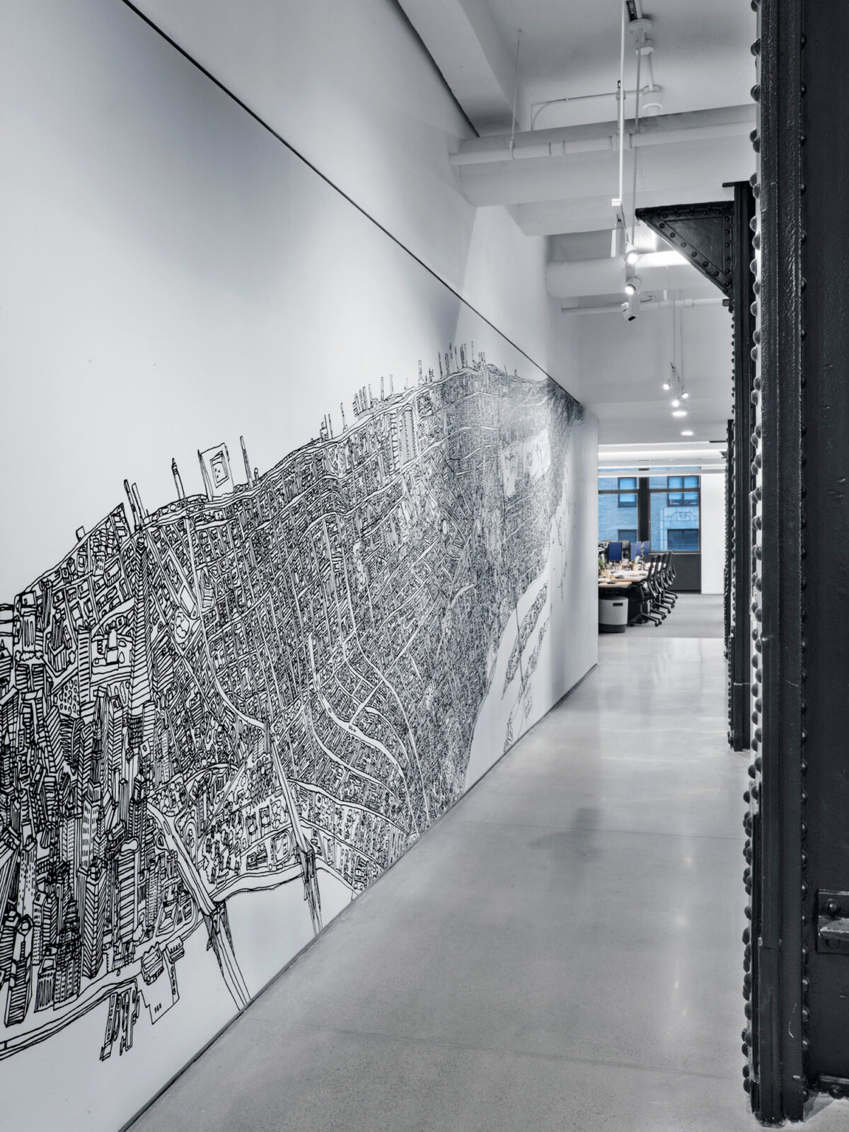A large, detailed wall mural depicting an intricate cityscape, enhancing the length of a well-lit corridor, leading to a bright office space with seating areas visible in the distance, showcasing an integration of art within a working environment.