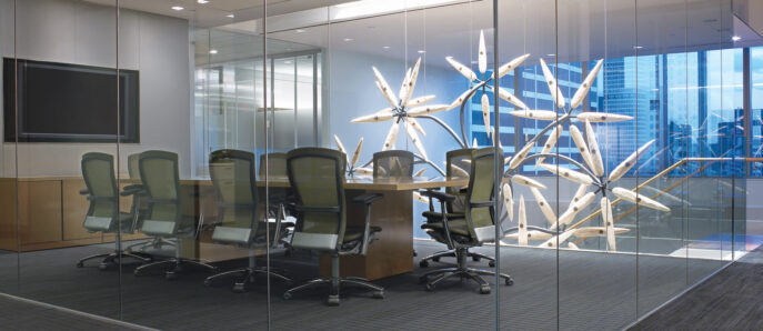 Modern conference room showcasing floor-to-ceiling glass walls, ergonomic black office chairs surrounding a sleek, rectangular meeting table, and dynamic geometric wooden sculptures adding an artistic focal point against the urban skyline background.