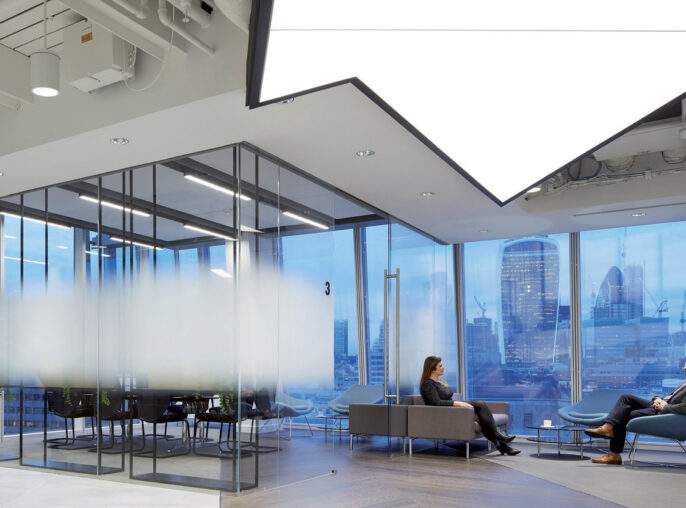 Modern office space featuring floor-to-ceiling glass partitions, sleek furnishings, and a neutral color palette. Ambient lighting complements the natural light flooding in from exterior windows, offering views of the urban skyline. Dynamic wood flooring contrasts with the structured ceiling design.