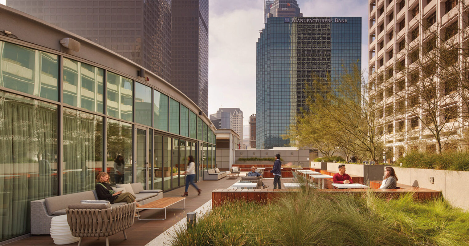 Rooftop terrace with contemporary outdoor furniture, strategic planters acting as natural partitions, and a view of urban skyscrapers under a clear sky. Occupants enjoy a blend of nature and cityscape in a harmonious, open-air setting.