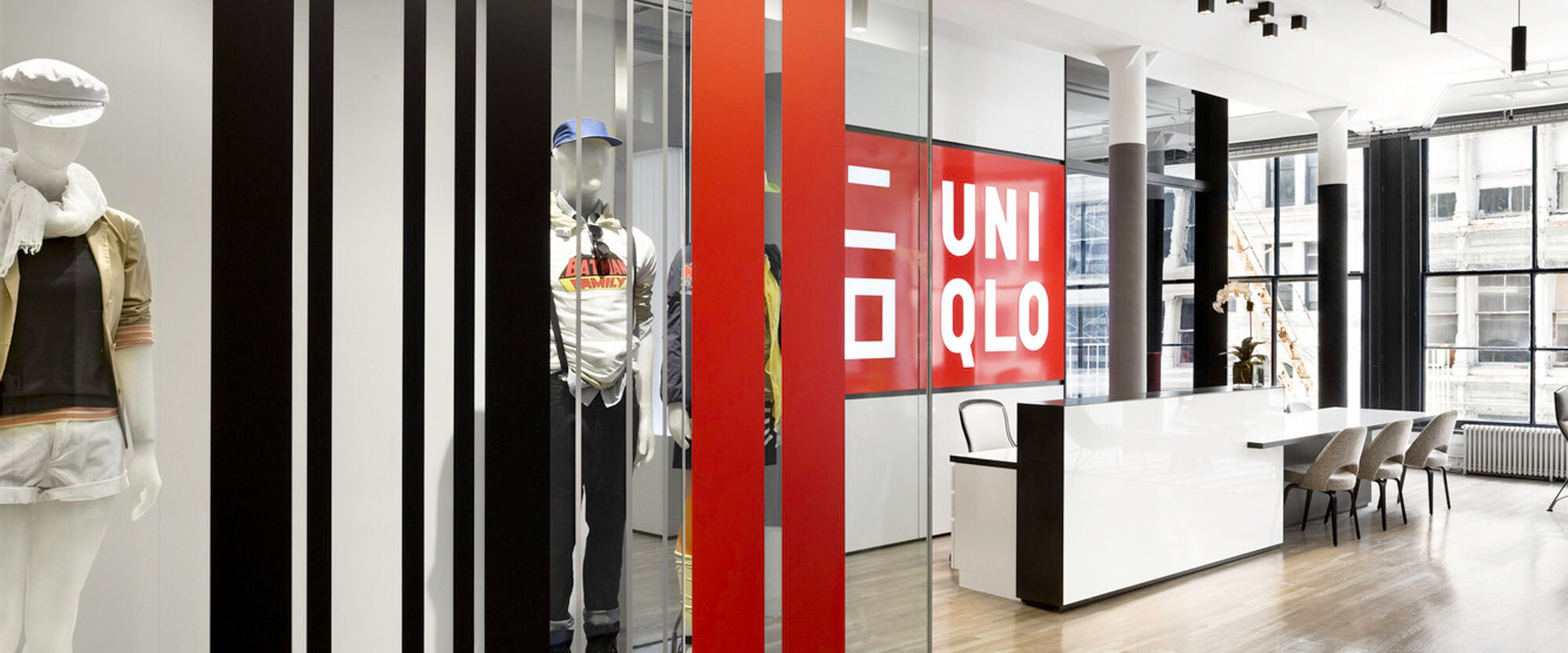 Modern retail interior featuring bold graphic black and red dividing elements, minimalist furniture, and a sleek white counter. Mannequins and large-scale branding enhance the contemporary atmosphere.