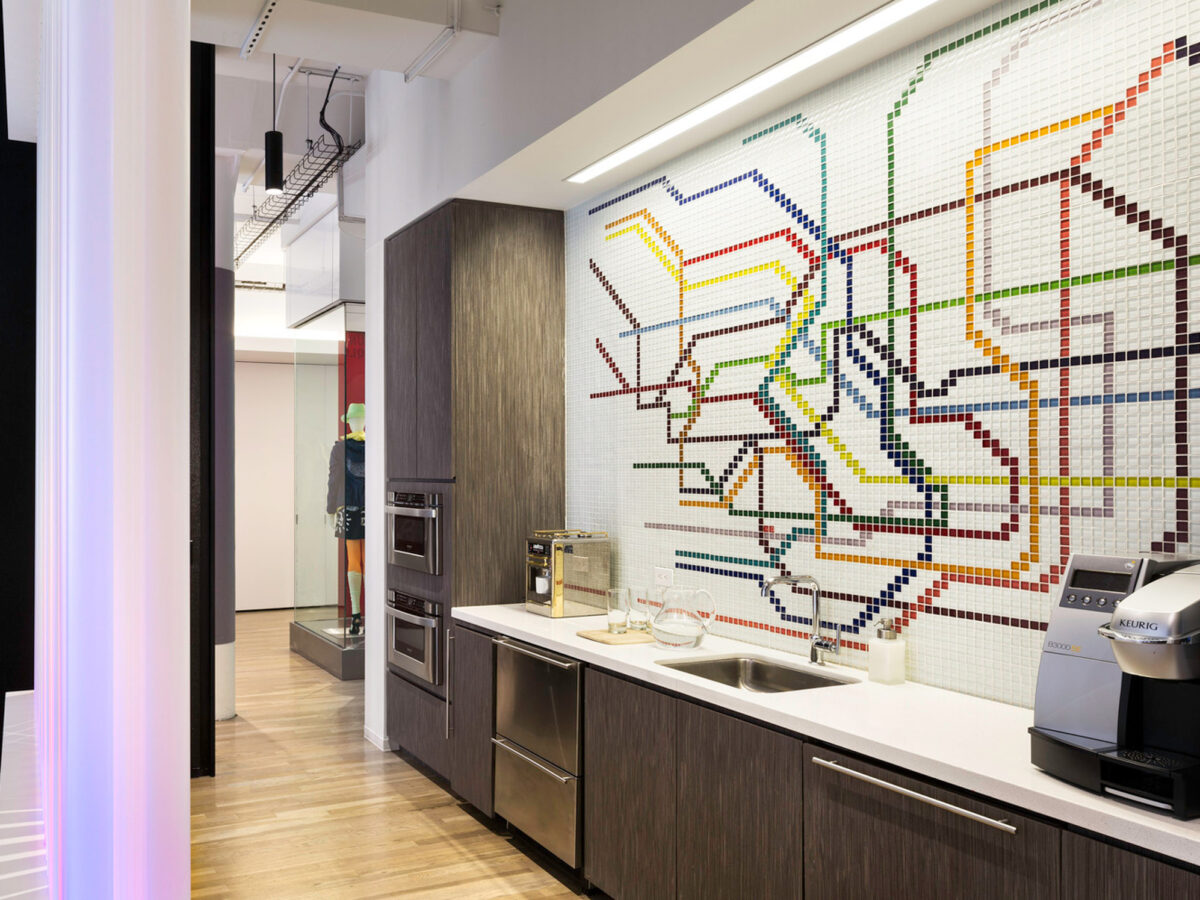 Contemporary kitchen with geometric mosaic backsplash, integrating neutral wood grain cabinetry and stainless steel appliances. Vertical LED accent lighting enhances the space's visual depth, juxtaposed with exposed ceiling infrastructure.