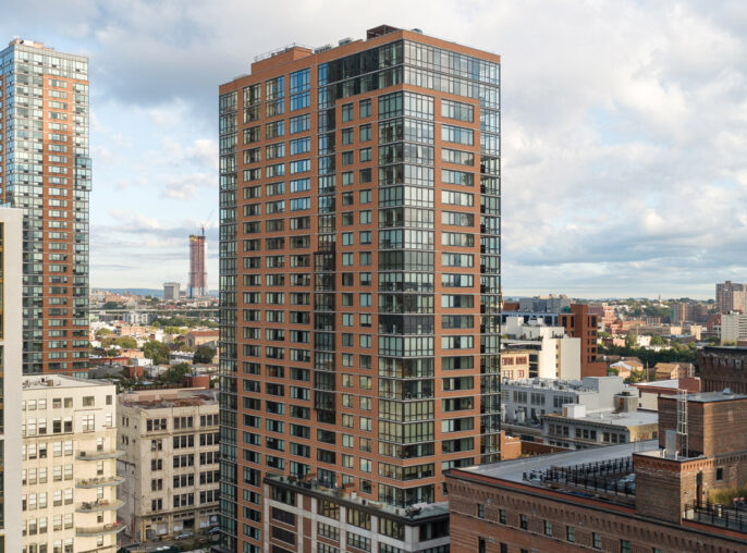 Modern urban landscape showcasing a mix of high-rise residential buildings with varied architectural styles, including glass facades and terracotta-colored brickwork, under a dynamic sky with scattered clouds.