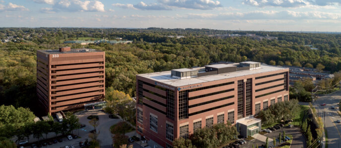 Elevated view of a modern office building complex with a symmetrical brick facade, surrounded by a landscaped parking lot and mature trees, highlighting suburban commercial architecture.