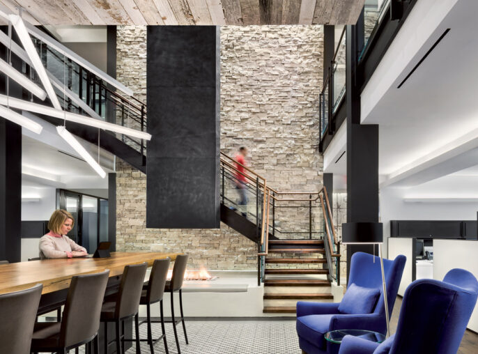 Modern interior design featuring a contrast of textures with exposed wooden beams, stone accent walls, and a geometric tiled floor. Sleek black metal staircases connect multi-level spaces, while royal blue armchairs add a pop of color to the predominantly neutral palette.