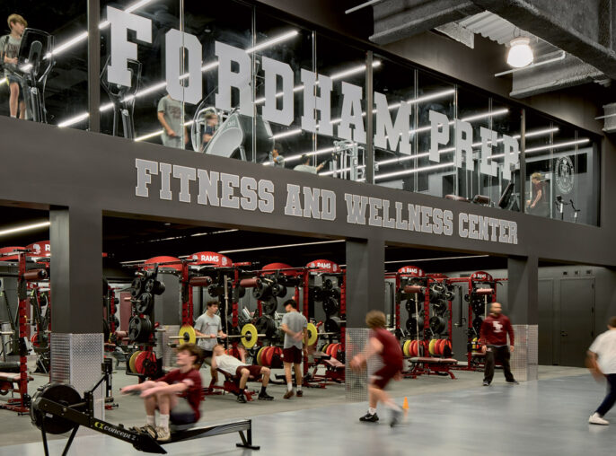 Spacious gym interior with exposed ductwork overhead, reflecting an industrial design. Mirrored walls amplify the space, featuring branded graphics for Fordham University. Red and black gym equipment are organized for functional training, promoting a vibrant, energetic atmosphere.