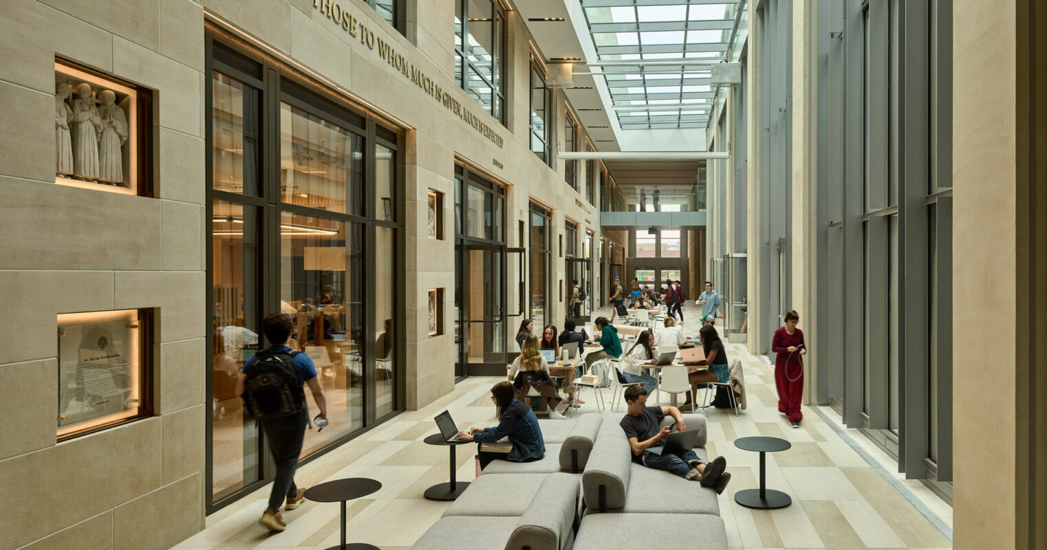 Spacious atrium embraced by natural light, featuring high ceilings, elongated windows, and a neutral color palette. Furnished with modular seating and round side tables, the space encourages casual gatherings amidst gallery-like walls adorned with framed exhibits.