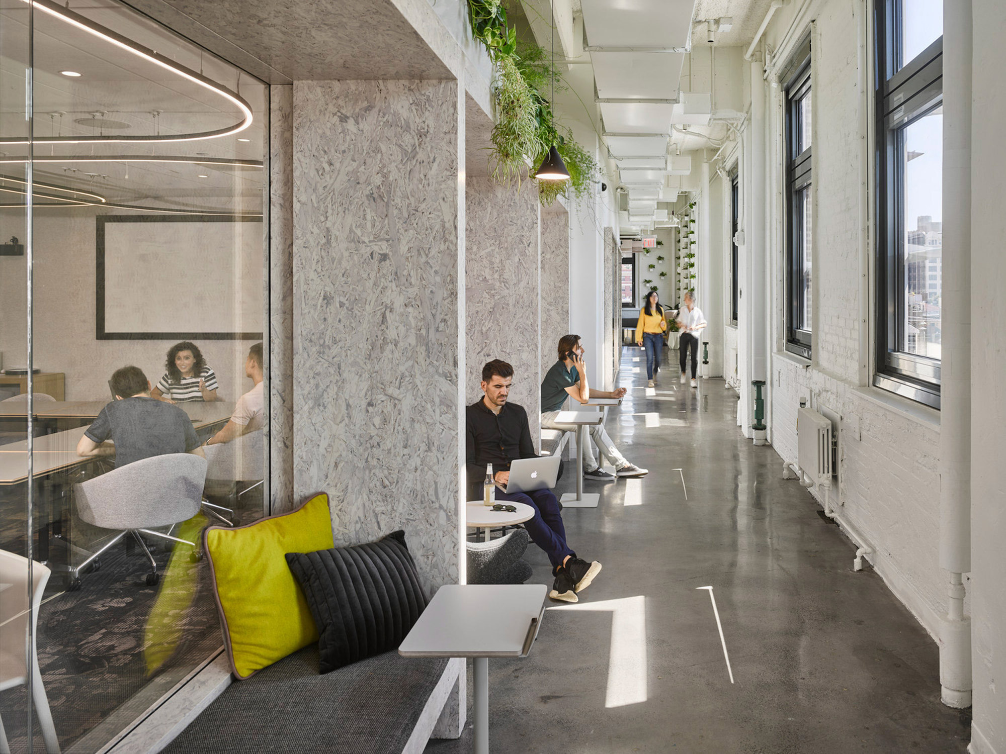 Modern office space blending natural light with greenery. Features a minimalist desk setup against marble walls, with employees working in communal zones that foster collaboration. Transparent partitions enhance openness, while plants add a biophilic touch to the sleek, contemporary environment.