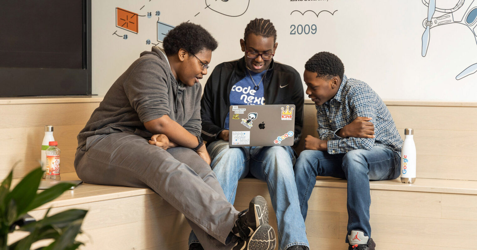 Three individuals collaborate in a casual office setting, highlighting a blend of creativity and comfort with a wooden bench, colorful wall graphics, and modern décor, projecting an innovative workspace atmosphere.