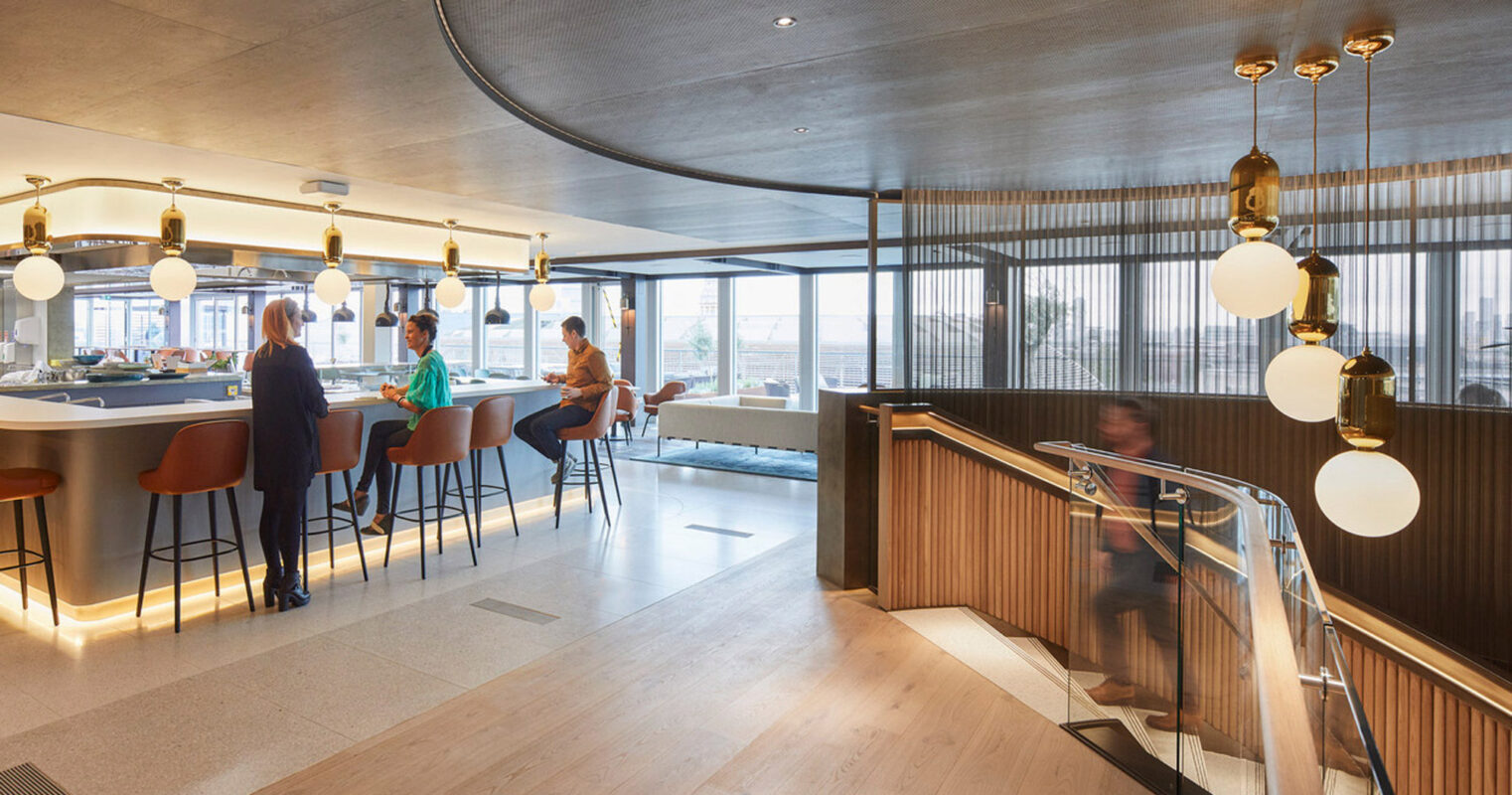 Modern bar interior with curved wood paneling, central island seating, hanging globe lights, and a welcoming ambiance. Patrons enjoy refreshments while conversing, illustrating a blend of functional design and social space.