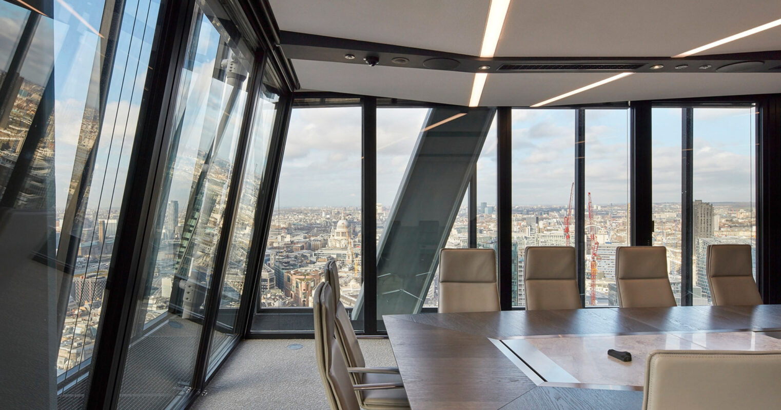 Modern conference room with panoramic city view, featuring floor-to-ceiling windows, a sleek, rectangular table, and comfortable chairs. The room is accentuated by minimalistic light fixtures and a dark grey carpet, emphasizing functional elegance.