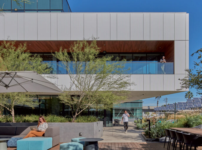 Modern architecture featuring a cantilevered building with clean white facades, expansive glass windows, and an integrated outdoor seating area with contemporary landscaping and hardscaping elements.