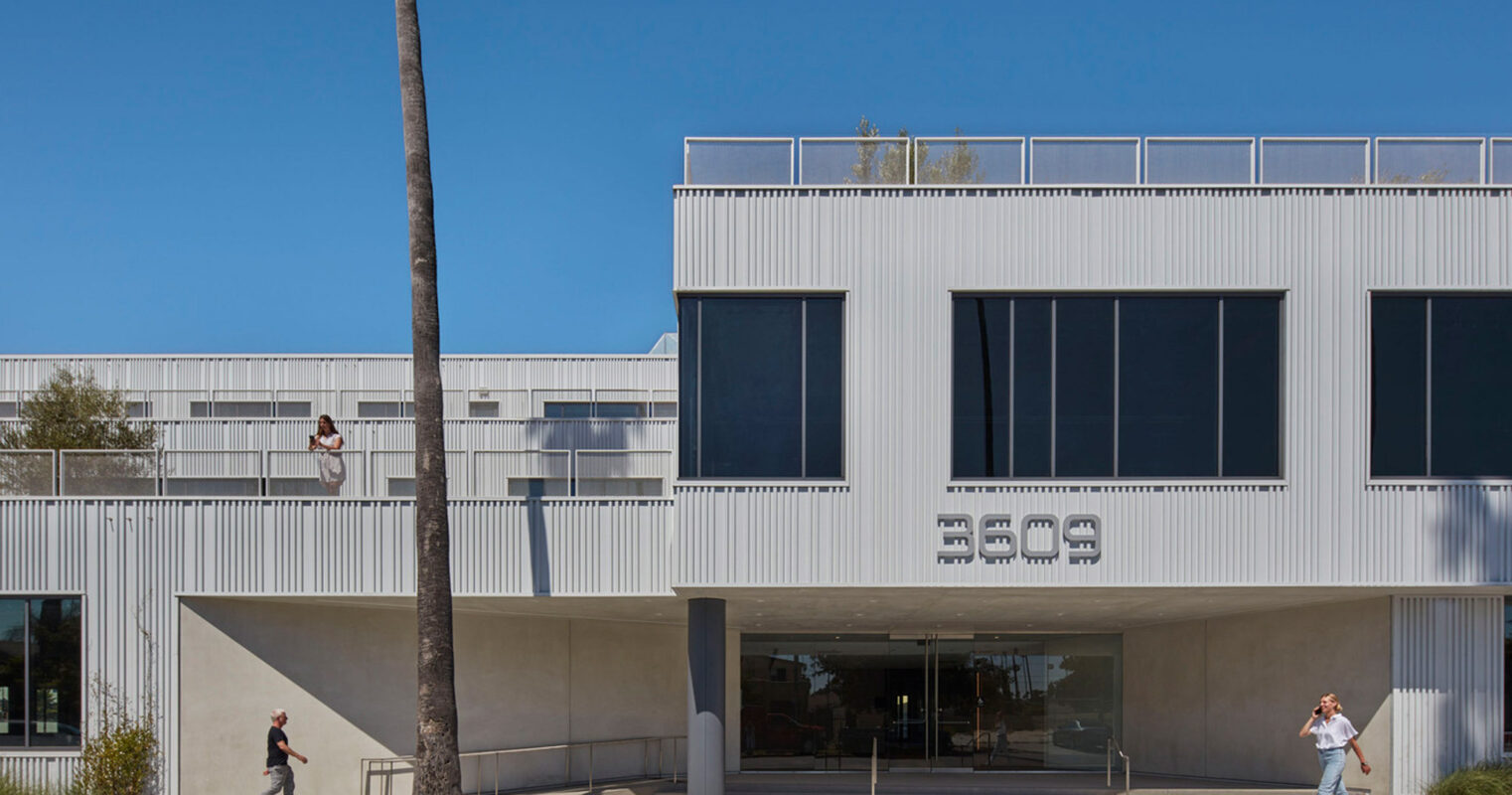 Modern architectural building facade featuring rhythmic metal cladding and a recessed entrance, flanked by mature palm trees and pedestrians for scale.