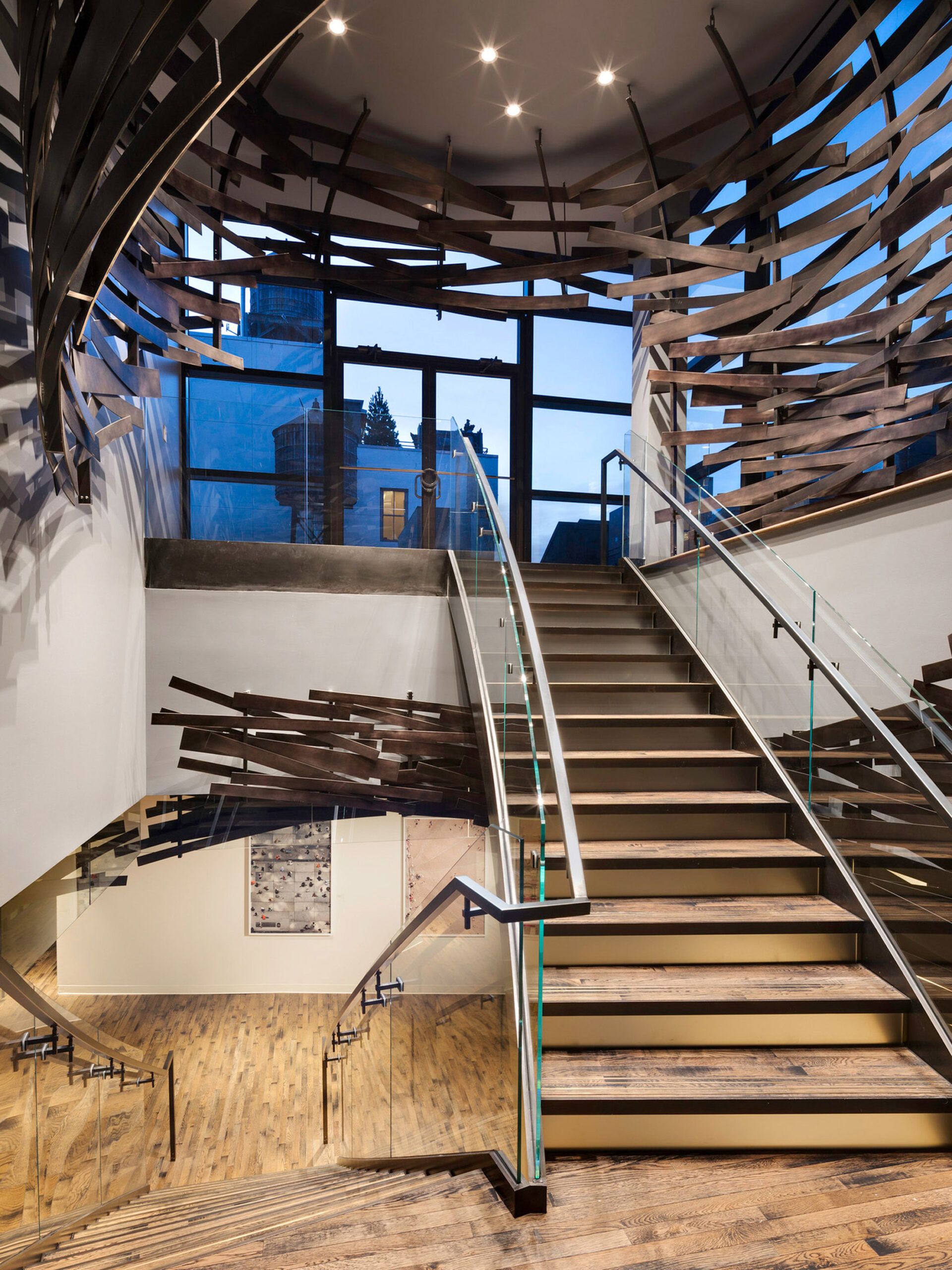 Modern staircase with floating wooden steps, complemented by a sculptural, slatted wood and metal railing that spirals upward, enhancing the space with dynamic lines and a play of light and shadow.