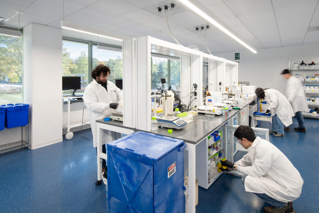 Bright, modern laboratory featuring spacious workstations equipped with laboratory equipment and supplies. Researchers in white lab coats actively engage in experiments, emphasizing collaboration. Large windows allow natural light, enhancing the workspace's functionality. Sleek designs and organized storage contribute to an efficient and professional research environment.