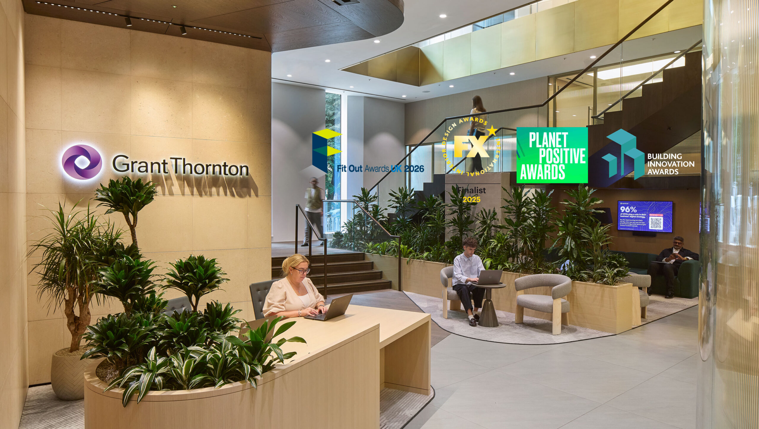 The spacious reception area of Grant Thornton features sleek wood paneling and modern furnishings. Lush greenery adds a touch of nature, while sophisticated lighting casts a warm glow. A prominent staircase leads to upper levels, enhancing visual interest and welcoming clients and guests into a refined workspace.