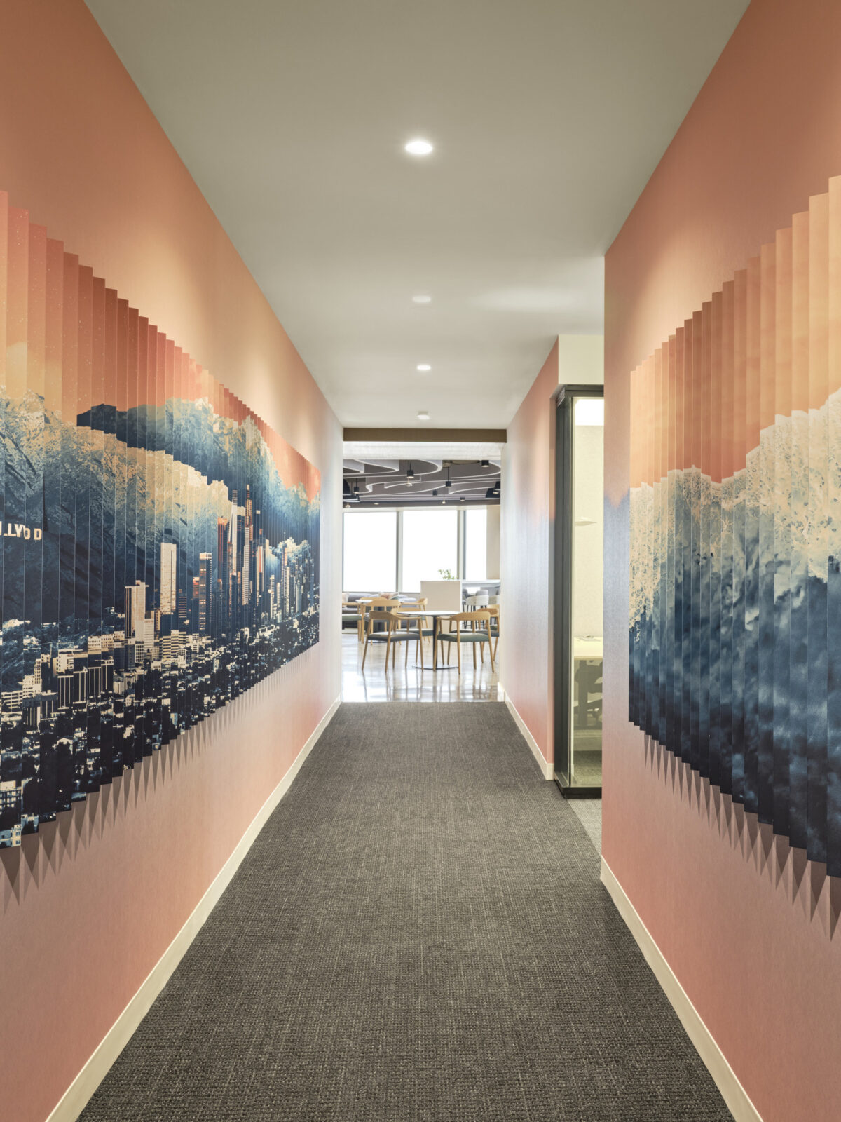 A narrow hallway featuring a striking wall mural depicting a stylized city skyline against a gradient background of soft pink and blue hues. The contrasting textures of the modern carpet and the smooth wall surface enhance the contemporary aesthetic, leading to a spacious, well-lit meeting area at the end.