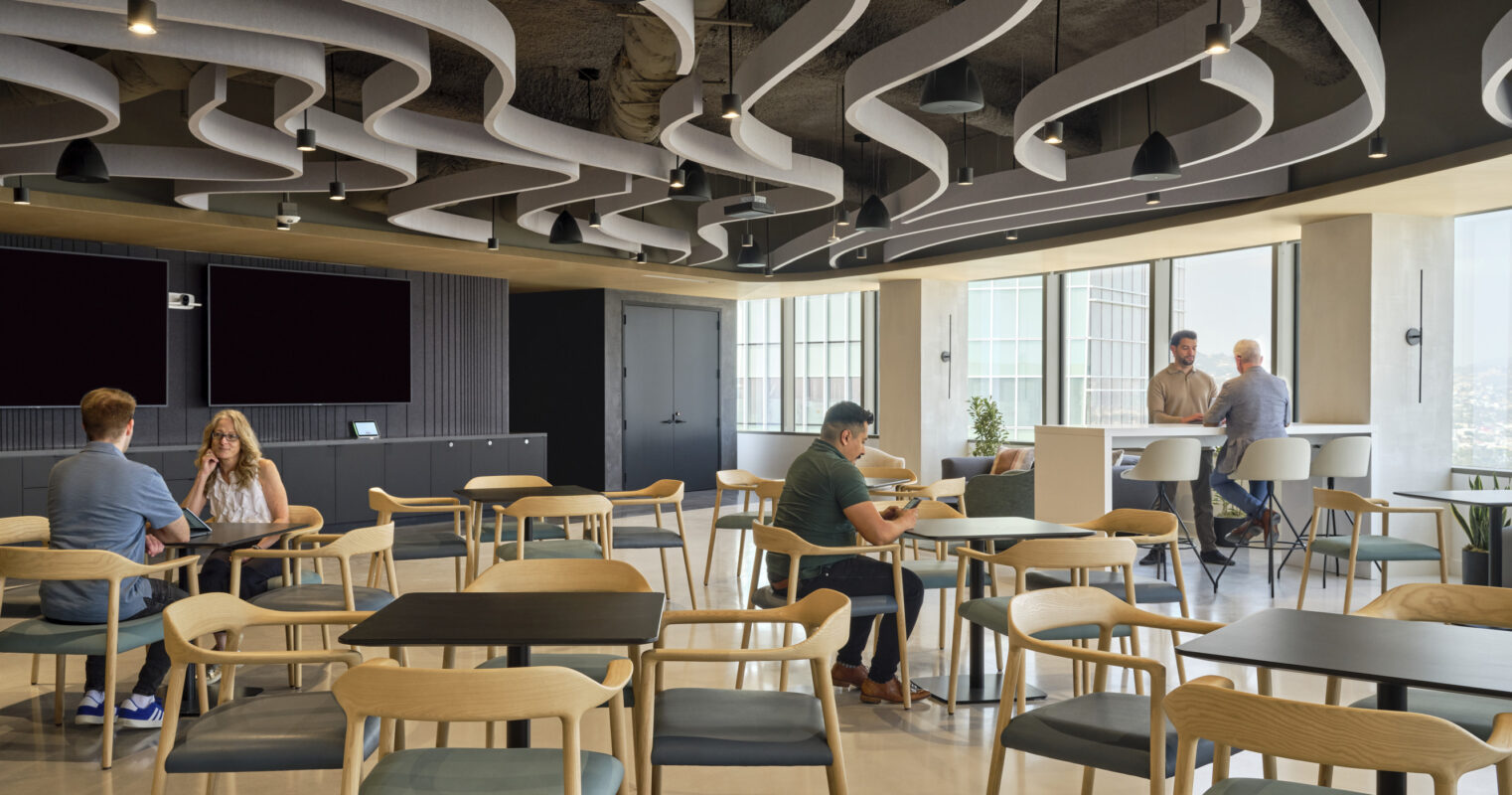 Modern office space featuring a contemporary design with fluid, sculptural ceiling elements that create visual interest. Natural light floods the area, enhancing the muted color palette of wood and grey tones. Flexible seating arrangements encourage collaboration and creativity among professionals, promoting a dynamic work environment.