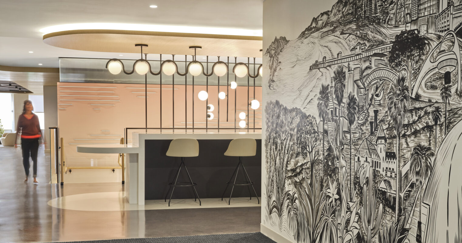 A modern office interior featuring a striking black and white mural depicting a cityscape. The open layout is complemented by sleek bar stools at a minimalist counter. Soft lighting from pendant fixtures enhances the contemporary ambiance, while a textured carpet adds warmth and depth to the space.