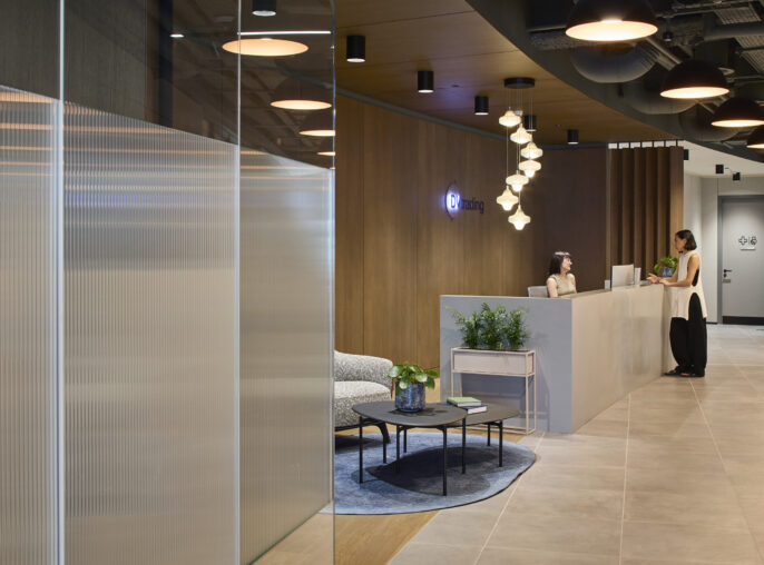 Modern reception area featuring sleek wood paneling and minimalist design. A reception desk offers a warm welcome, complemented by stylish seating and greenery. Unique pendant lighting creates an inviting atmosphere, while large windows allow natural light to enhance the space, promoting a sense of openness and professionalism.