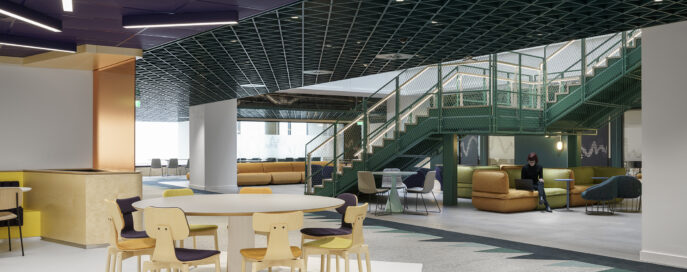 A contemporary open-plan interior showcasing a vibrant lounge area with green and gold accents. The design features a modern staircase leading to elevated seating areas, complemented by colorful chairs and a mixed-use table. Sleek geometric ceilings enhance the space, promoting a collaborative and inviting atmosphere.