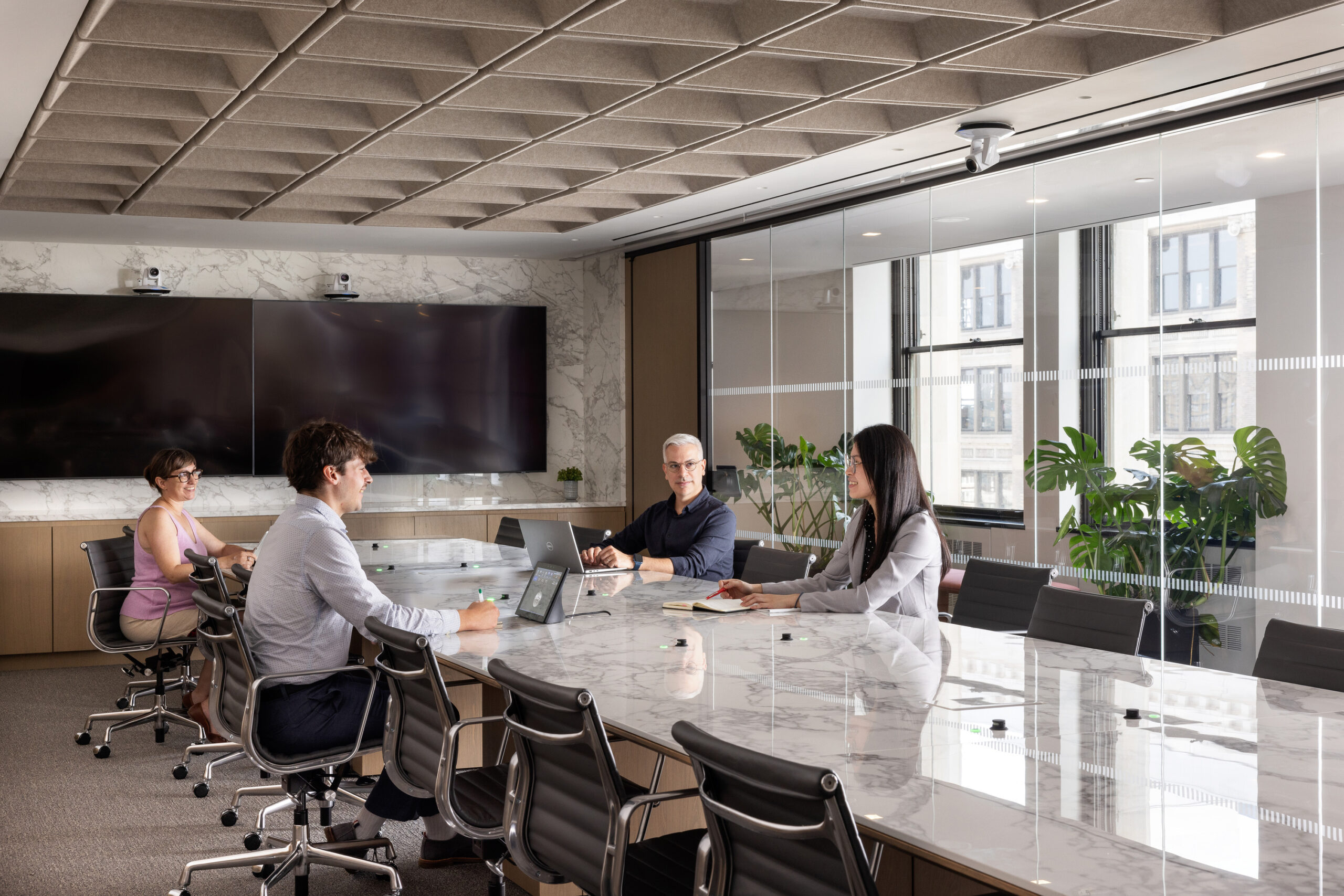 Modern conference room featuring a large marble table surrounded by ergonomic chairs. Natural light floods the space through expansive windows, highlighting the textured ceiling and elegant decor. Green plants add a touch of nature, creating a professional yet inviting atmosphere for collaborative discussions.