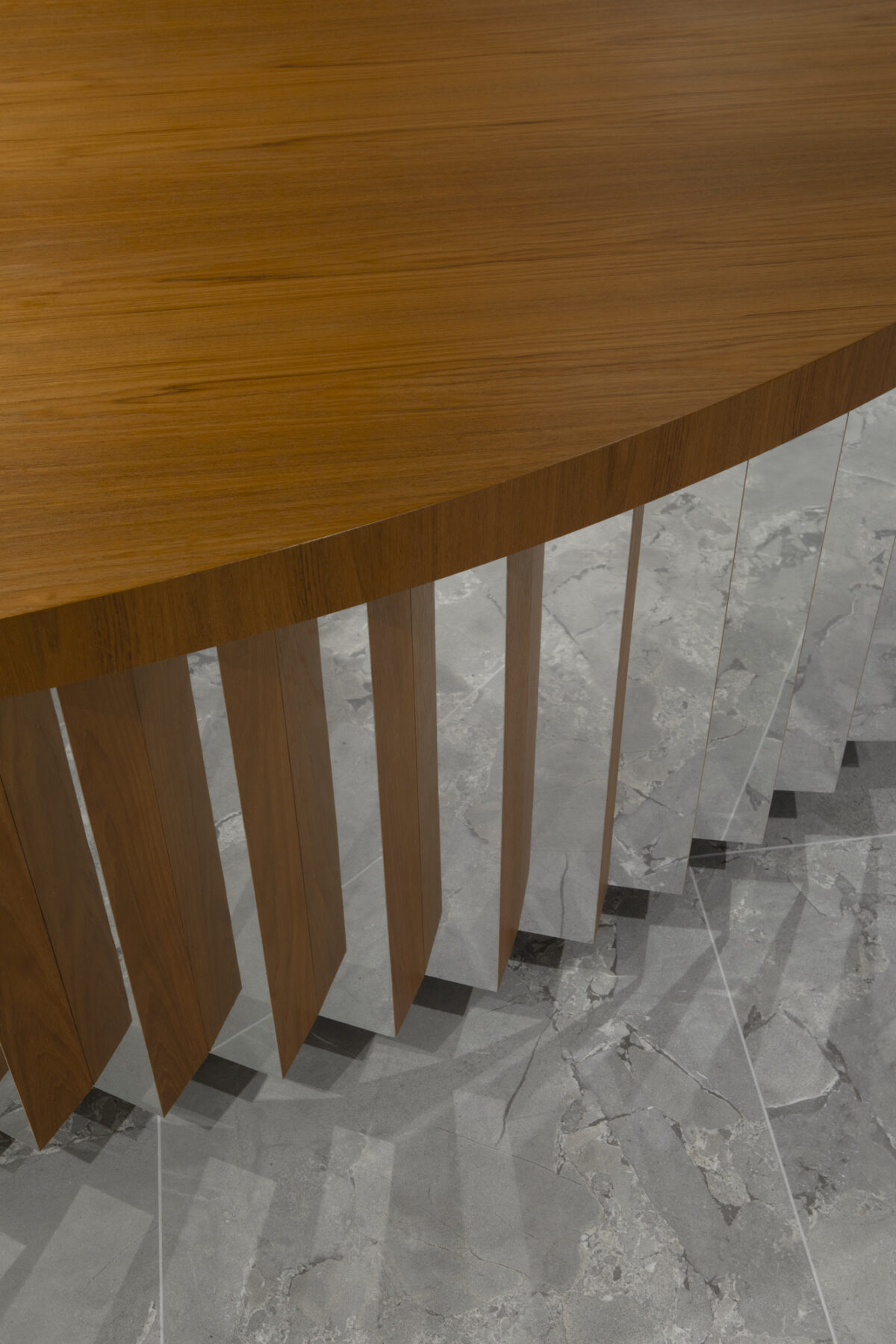 Curved wooden tabletop features intricate grain patterns, supported by a series of vertical wooden slats that taper elegantly. The contrast with the polished marble floor enhances the contemporary aesthetic, showcasing a harmonious blend of natural materials in a sophisticated interior design setting.