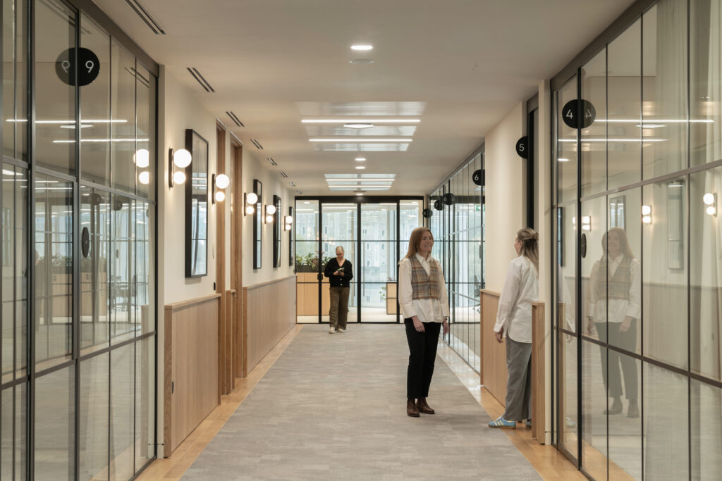 Interior view of a cooridor in a workplace with glass-fronted meeting rooms on either side of the hallway. Clear signage indicates the room numbers for ease of navigation. 