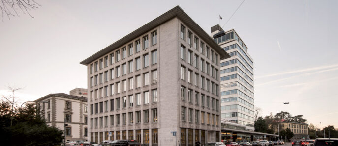 Corner view of a modern office building at dusk, showcasing a juxtaposition of robust square architecture with reflective glass windows, set against a softening twilight sky.