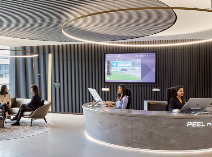 Modern corporate lobby with a curved, sleek reception desk, ambient lighting from a circular ceiling feature, and wood-paneled walls. Comfortable seating areas and large screen display enhance the welcoming atmosphere.