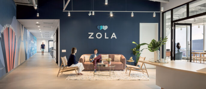 Spacious corporate interior features an exposed concrete ceiling with suspended linear lighting, enhancing a modern industrial aesthetic. Rich navy walls contrast with warm wooden accents and a bespoke wall mural, while contemporary furniture provides casual seating areas for collaboration. Strategic placement of indoor plants introduces a natural, calming element within the workspace.